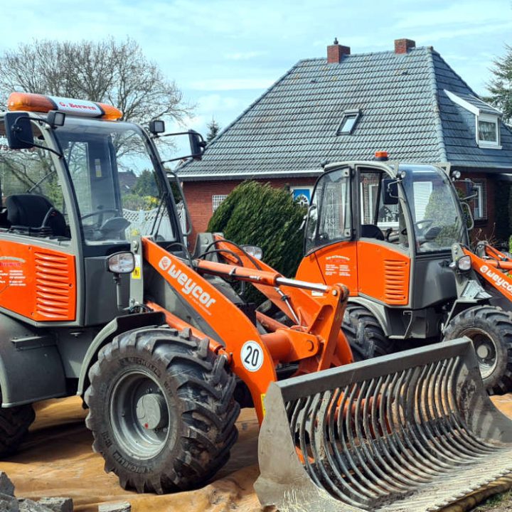 Zwei orange Radlader der Marke Weycor bei Pflasterarbeiten vor einem Einfamilienhaus.